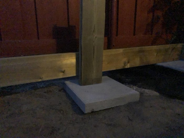 Betongplatta med trästödben mot regel för altanbygge vid skymningen.