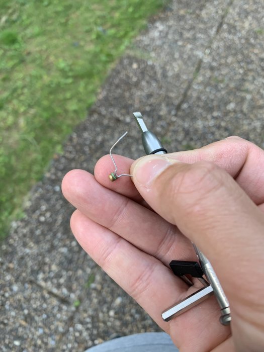 Hand håller en temperaturgivares trådar och motstånd vid en reparation utomhus.