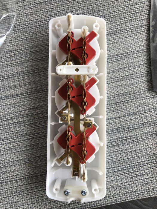 Öppnat jordat grenuttag med synliga anslutningar för jord, fas och noll för installation genom bokhylla.