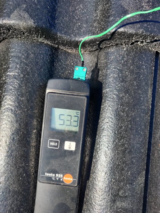 Termometer som visar 53.3 grader Celsius på en svart yta.