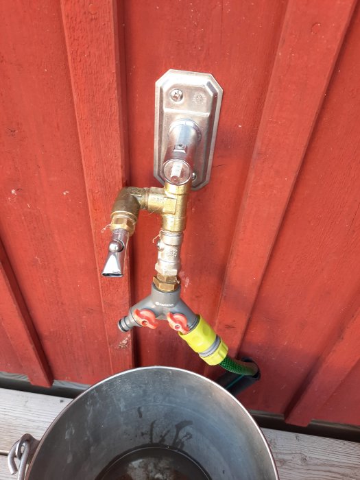 Bitkulventil monterad på röd vägg med hink under, begränsar vattenflödet för barnens lek.