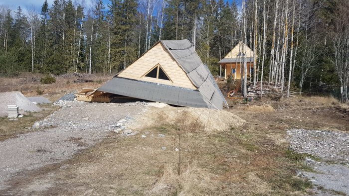 Halvfärdigt hus med svart takpapp och byggmaterial omkring på ojämn tomt.