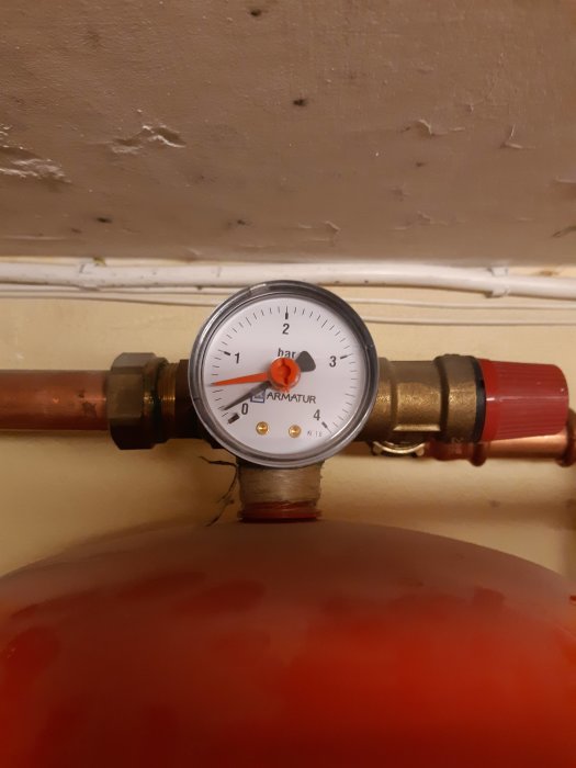 Tryckmätare på en rörledning över en röd expansionskärl visar under 1 bar.
