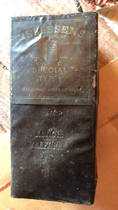 Gammal svart låda med text "Hellesens Drylement Special Typ 1 Elektromof kraft 1,5 Volt".