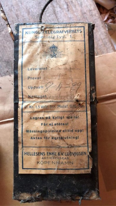 Gammal etikett på en låda med text "Kungliga Telegrafverkets Speciale Typ 1" och varningsinstruktioner, nött och smutsig.