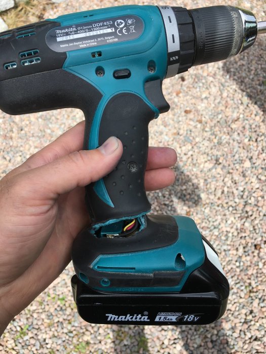 Hand håller en trasig Makita skruvdragare med sprucken plast vid handtaget, märkt "Made in China".