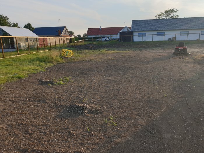 Nypreparerad trädgårdstomt i skymningen med odlingsväxthus i bakgrunden och en gräsklippare i förgrunden.