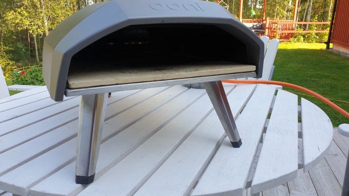 Portabel pizzaugn placerad på ett vitt runt bord utomhus.