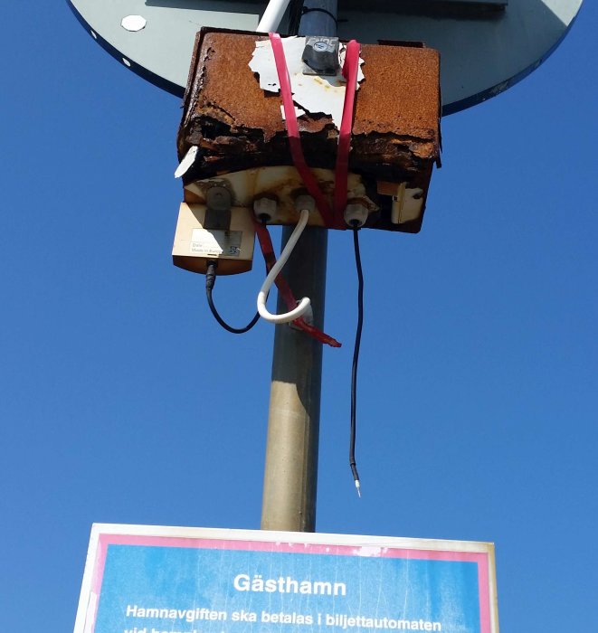 Rostigt skåp med kablar på stolpe över skylt för Gästhamn i Bovallstrand.