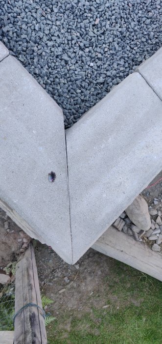 Närbild på en nyligen konstruerad hörndel av en betongmur med grus bakom och en träplanka nedanför.