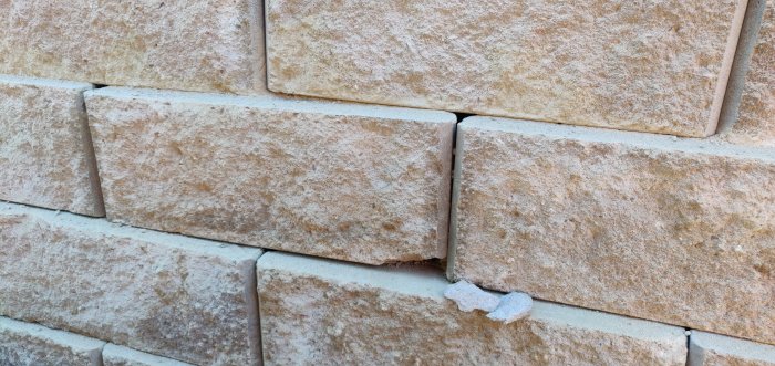 Närbild av ny mur med ojämnt lagda stenblock och synlig fogmassa.