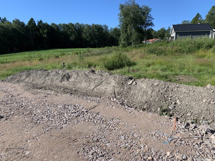 Byggarbetsplats med jordhögar och grus för breddning av planen inför rördragning.