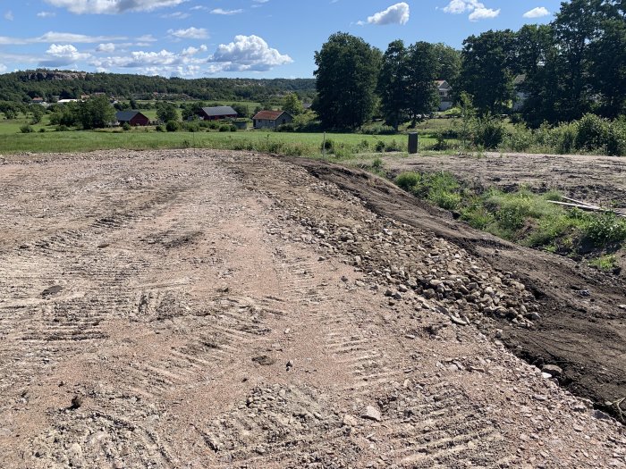 Jordfyllnad på byggplats för återfyllning och utrymme för dagvatten och dränering, med omgivande natur.