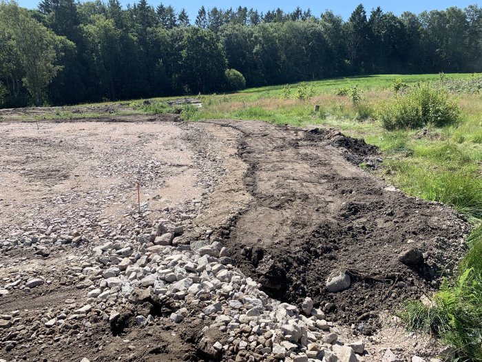 Jordfyllnad bredvid en planerad yta för byggprojekt med plats för dagvattenhantering och dränering i ett soligt landskap.