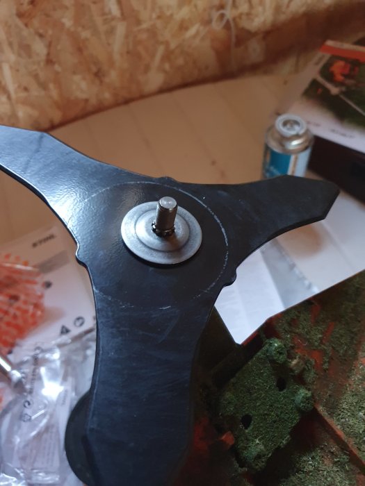 Del av röjsågsklinga med en monterad mutter, placerad inomhus med arbetsmaterial i bakgrunden.