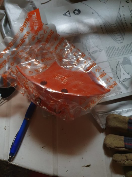 Orange skyddslock för STIHL FS 240 C i plastförpackning med instruktionsmanual och penna på ett bord.