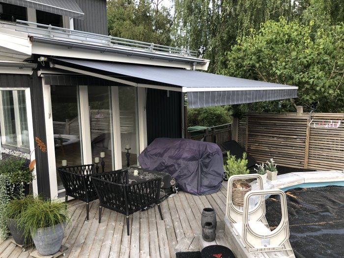 Nyinstallerad grå markis över uteplats på husets baksida med trädgårdsmöbler och poolskydd.