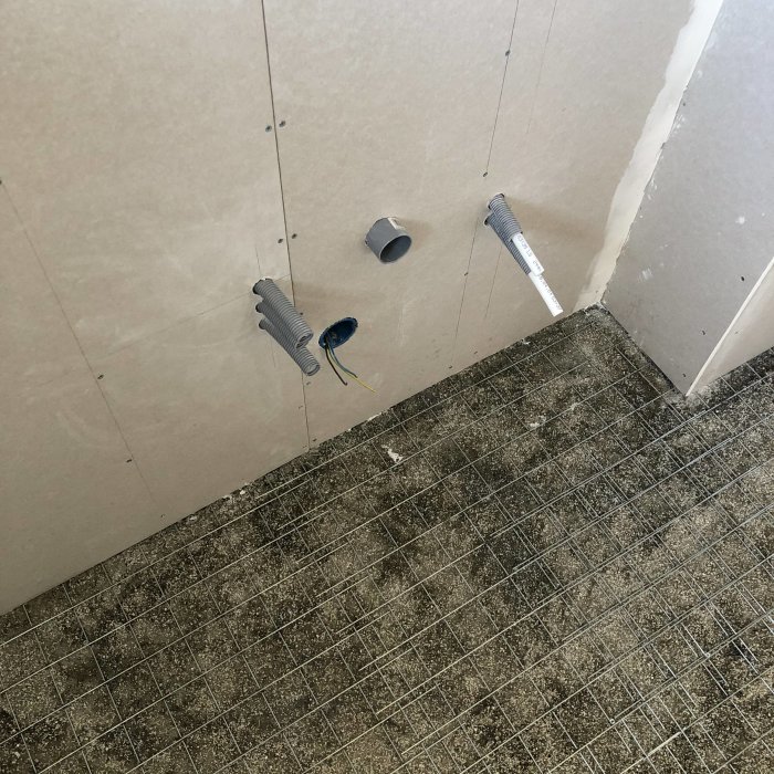 Vägg med hål borrade för rör och kablar, fogmassa kring en genomföring, på en byggarbetsplats.