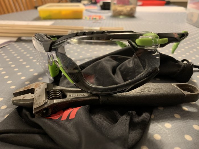 Skyddsglasögon och tång på en tygpåse, placerade på ett prickigt bord.