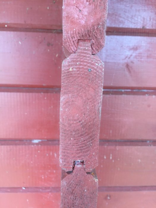 Närbild av ett trästycke med not och fjäder från en timmerstuga, målat i rött.