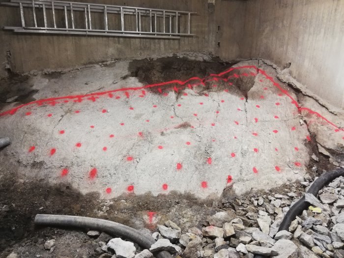 Betongyta markerad med röda streck och prickar för rivning, omgiven av grus och rör.