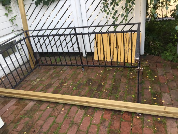 Rostigt smidesräcke från 30-talet bredvid en vit vägg och trädgårdsgång, behöver renovering.