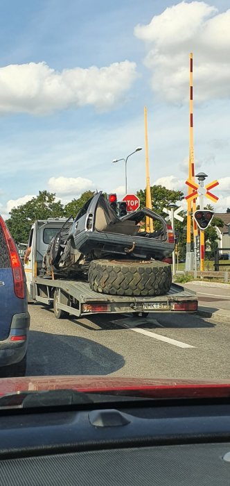 Biltransport med en överlastad och skadad bil på flak, osäkrad vid järnvägsövergång i Uppsala.