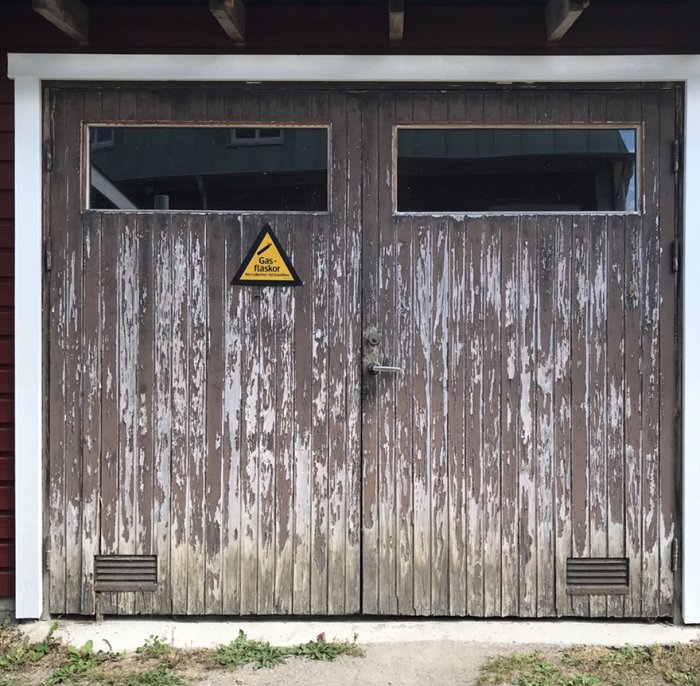 Slitet garage med två portar, avskalad färg och varningsskylt för gasflaskor, före renovering.