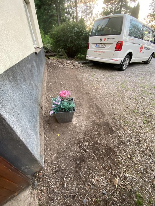 Renoverad trädgård med nyplanterade blommor vid husvägg och parkerad servicebil.