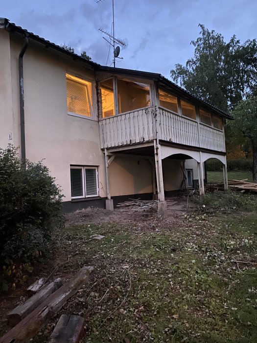 Suterränghus från 1960 med rensad vegetation och synliga renoveringsbehov på balkong och farstukvist.