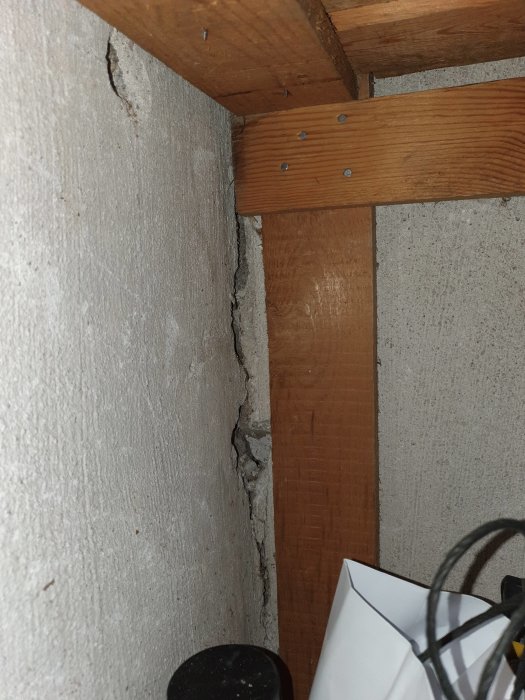 Synlig spricka i skarven mellan en betongvägg och en trästolpe i en källare.