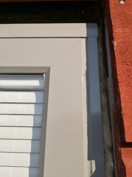 Närbild av ett fönsterhörn med vit karm mot en röd tegelvägg.