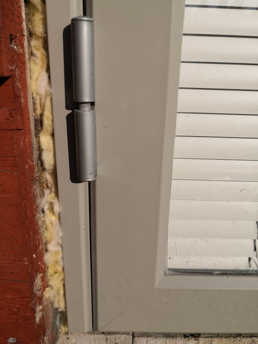 Närbild på ett dörrhörn med dörrgångjärn och isoleringsskum vid vägganslutning.