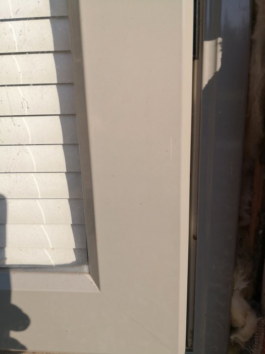 Närbild av hörnet där en vit dörr möter en fönsterkarm och persienn.