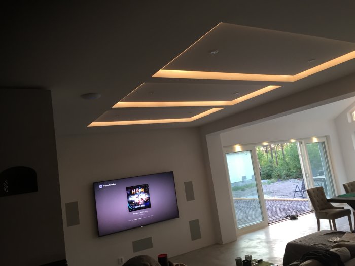 Modernt inrett vardagsrum med infällda LED-listar i taket och en stor TV på väggen.