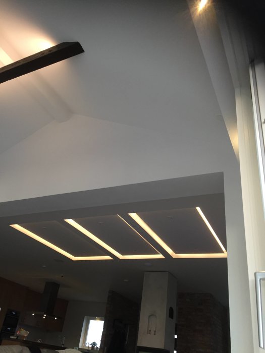 Tak med inbyggda LED-listor i ett modernt kök, del av ett hemmasnickrat bord syns.