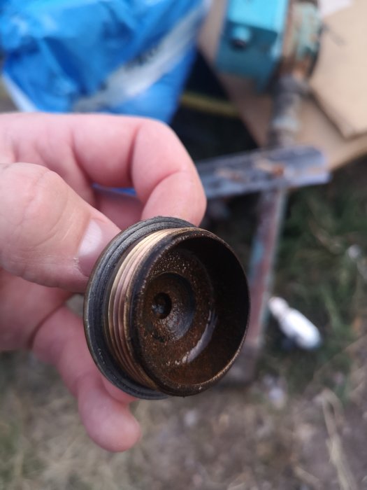 Hand håller ett rostigt lock med en synlig packning på insidan.
