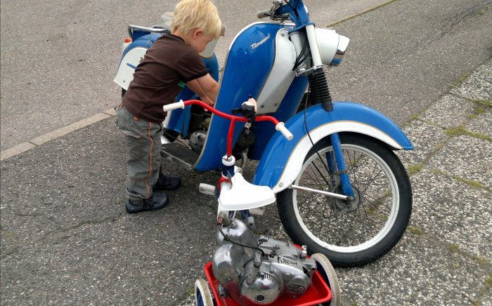 Barn justerar styret på en leksaksmoped bredvid en verklig veteranmoped.