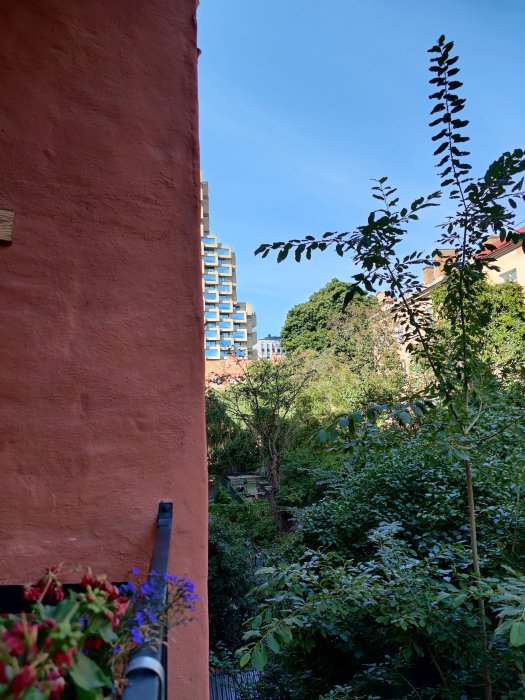 Utsikt från en balkong med grönska och moderna byggnader i bakgrunden.