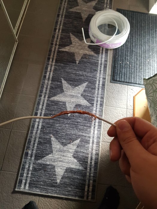 Hand håller sönderrostat elkabel framför trasmatta på golv.