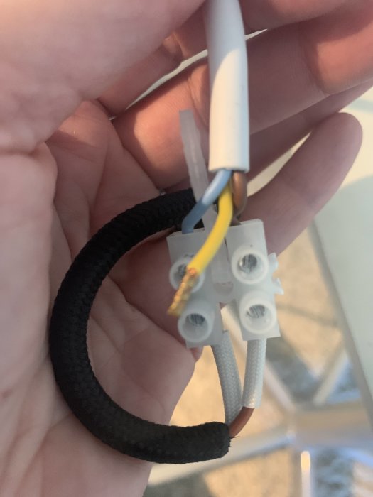Hand håller en taklampas elkabel med en blå och brun tråd ansluten till en sockerbit och en oansluten gul/grön skyddsjord.