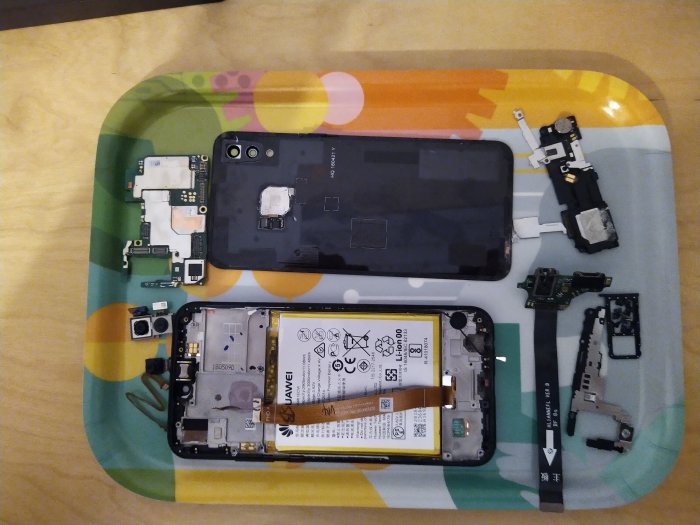 Öppnad mobiltelefon med avlägsnat bakstycke och exponerade interna komponenter på ett mönstrat underlag.