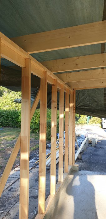 Trästomme i garage under reparation med synliga skarvar och potentiell rötskada i gamla bjälkar.