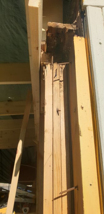 Ny träbjälke skarvad med gammal, delvis rutten stomme med spik. Potentiellt stabilitetsproblem.