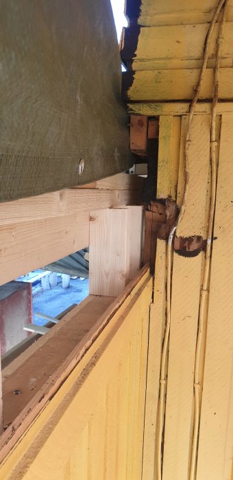 Delvis synlig träkonstruktion visar en skarvad bjälke som vilar på en troligtvis rötskadad stomme, vilket ifrågasätts för dess säkerhet.