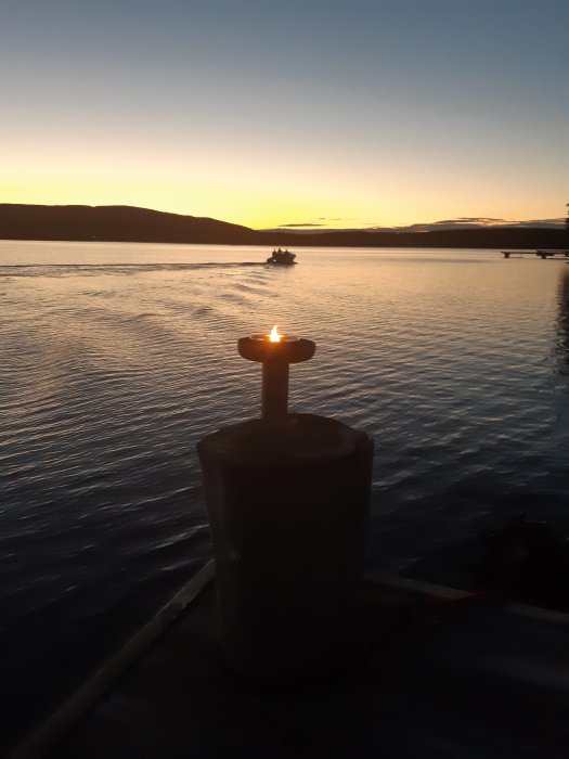 Solnedgång över vattnet med en tänd ljusstump på en brygga och en båt i fjärran.