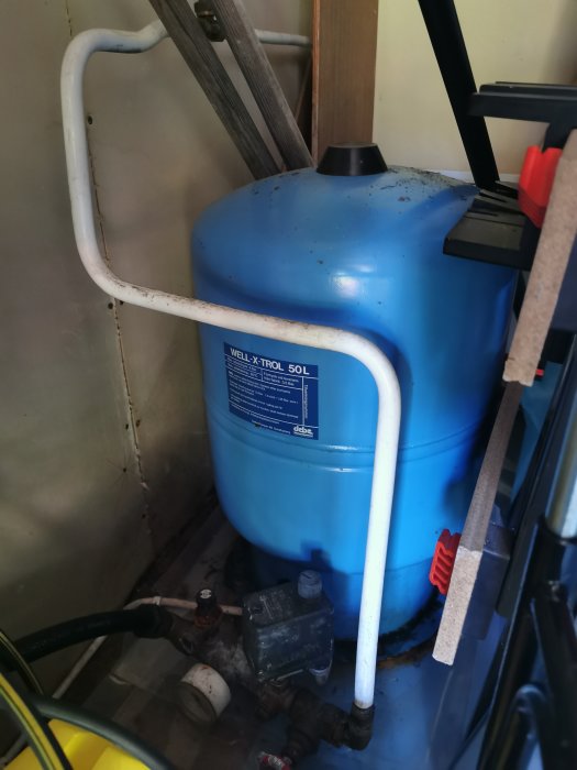 Blå hydrofortank märkt med Well-X-Trol och vred i ett husförråd, tillsammans med rör och ventiler.