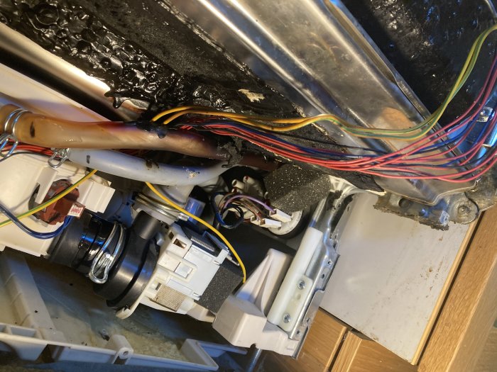 Elektriska kablar och slang under diskmaskin, med tejp och kladd, undersöks för skador.