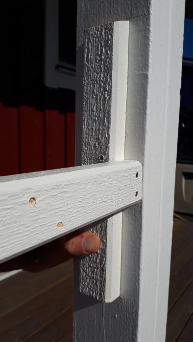 Hand som håller en vit målad lockläkt monterad horisontellt mellan två vita kvadratiska stolpar på en balkong.