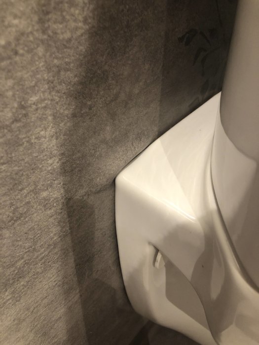 Renoverat badrum med vägghängd wc och grå plastmatta, synliga fuktskador intill toaletten.